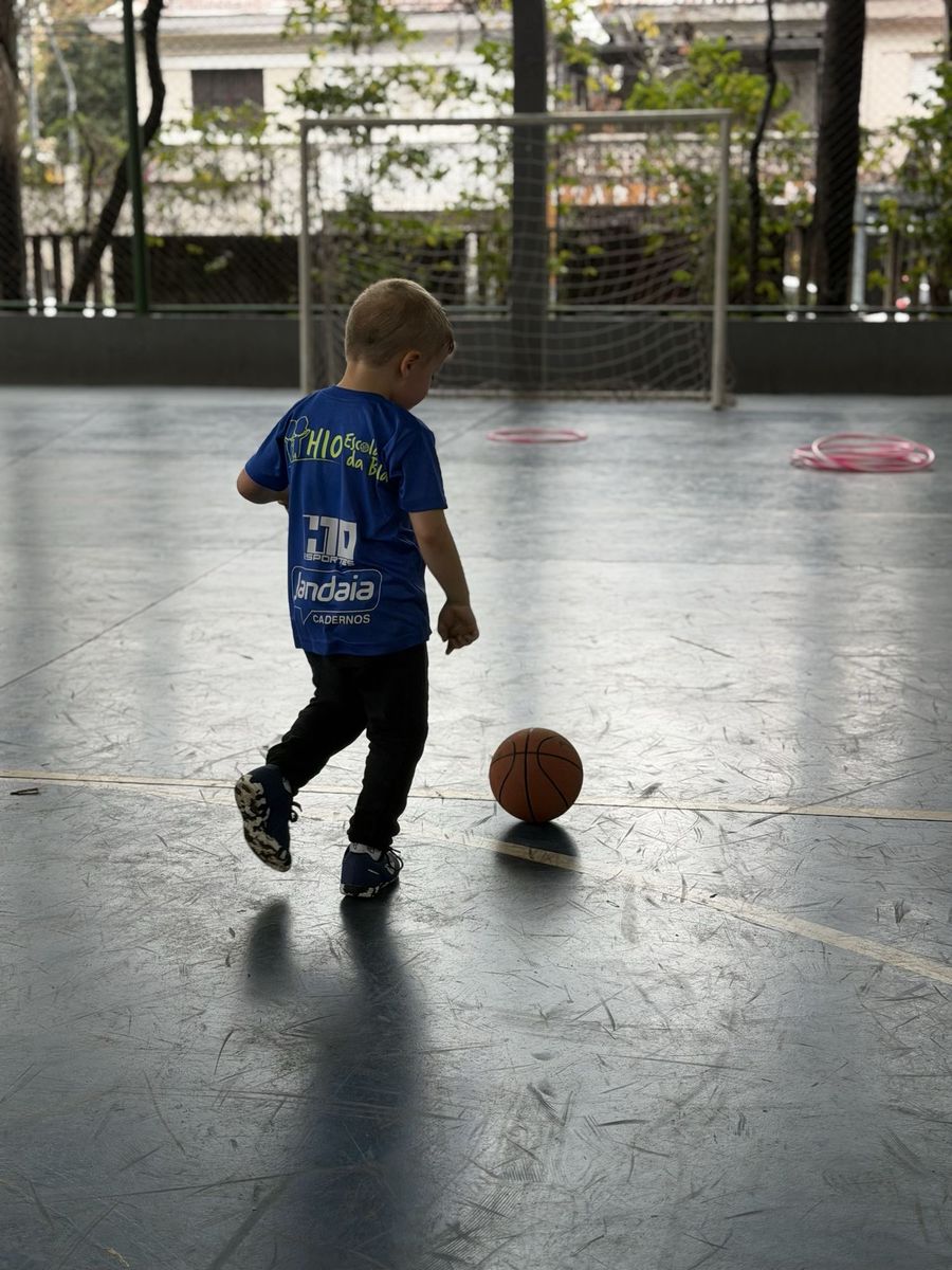 Menino do H10 Kids caminhando de costas até a bola, na quadra coberta do Baetinga