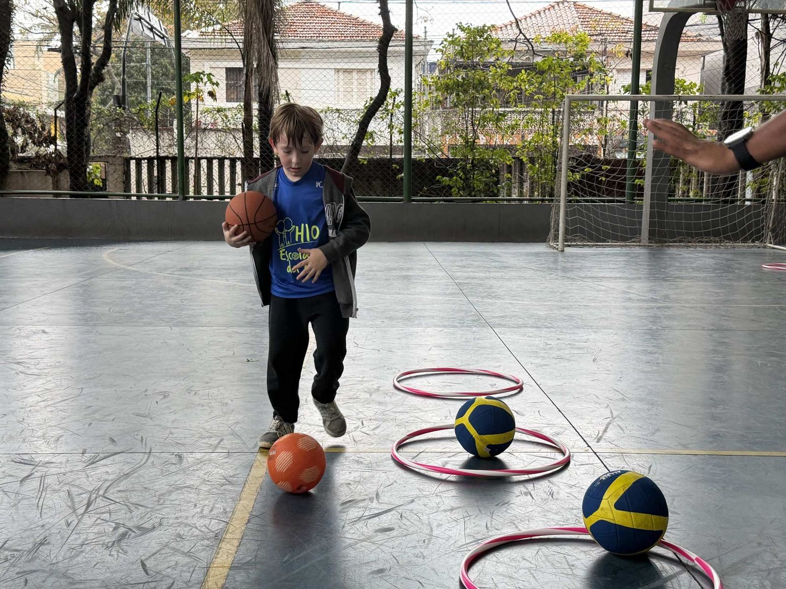 Menino do H10 Kids conduzindo a bola entre arcos e bolas de esportes diferentes